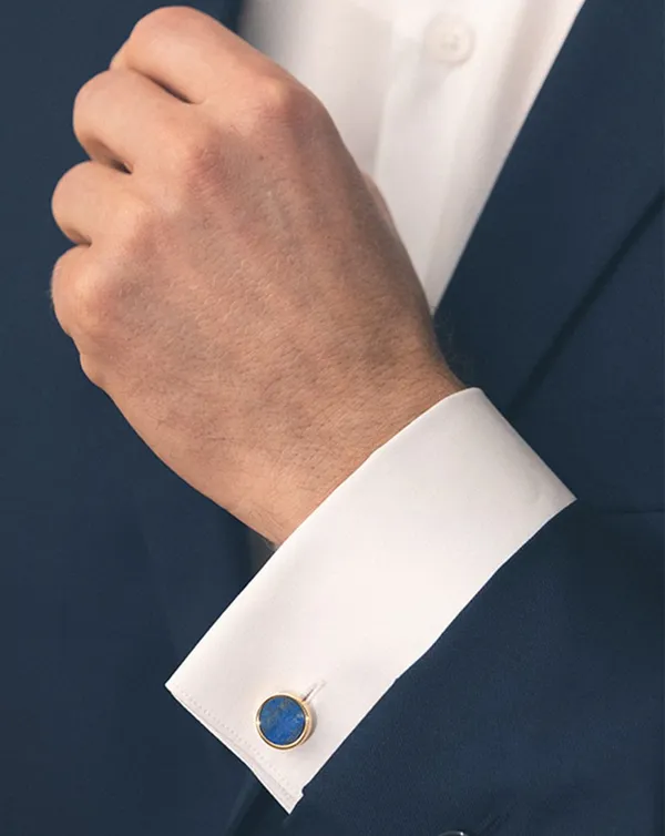 Homme en costume bleu portant des boutons de manchette dorés et bleus.
