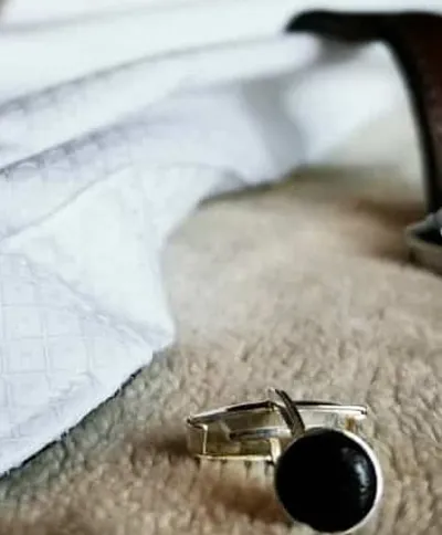 Bouton de manchette noir sur tissu beige et chemise blanche.