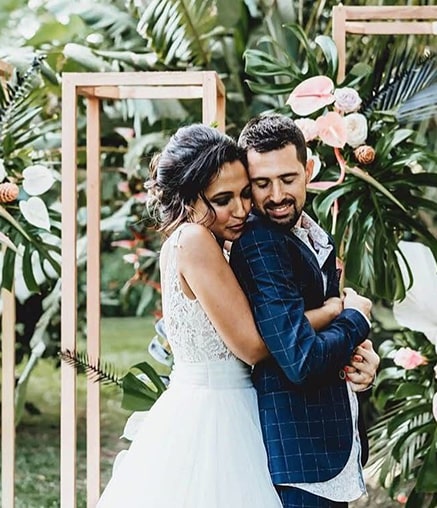 Couple en tenue de mariage s'embrassant devant une arche florale.