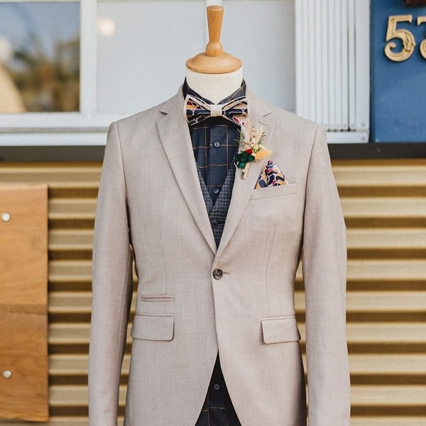 Mannequin portant un costume beige avec nœud papillon et boutonnière.