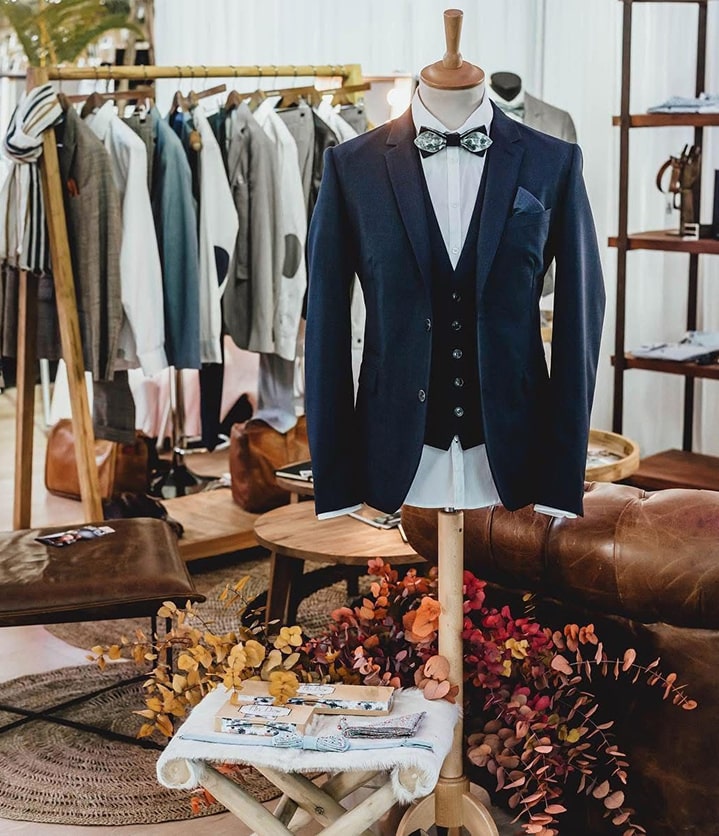 Mannequin portant un costume avec nœud papillon, vêtements en arrière-plan.