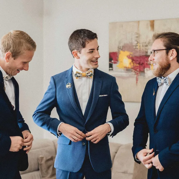 Trois hommes en costume bleu discutent, portant des nœuds papillon assortis.