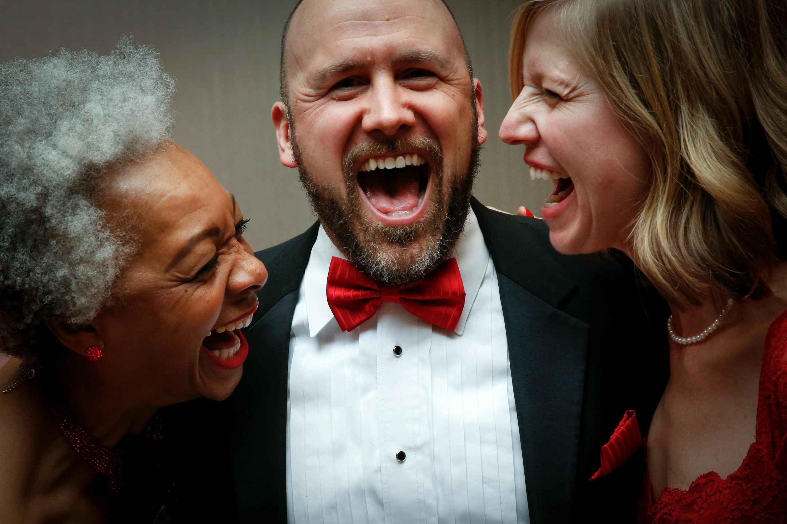 Trois personnes élégantes rient ensemble en tenue de soirée.