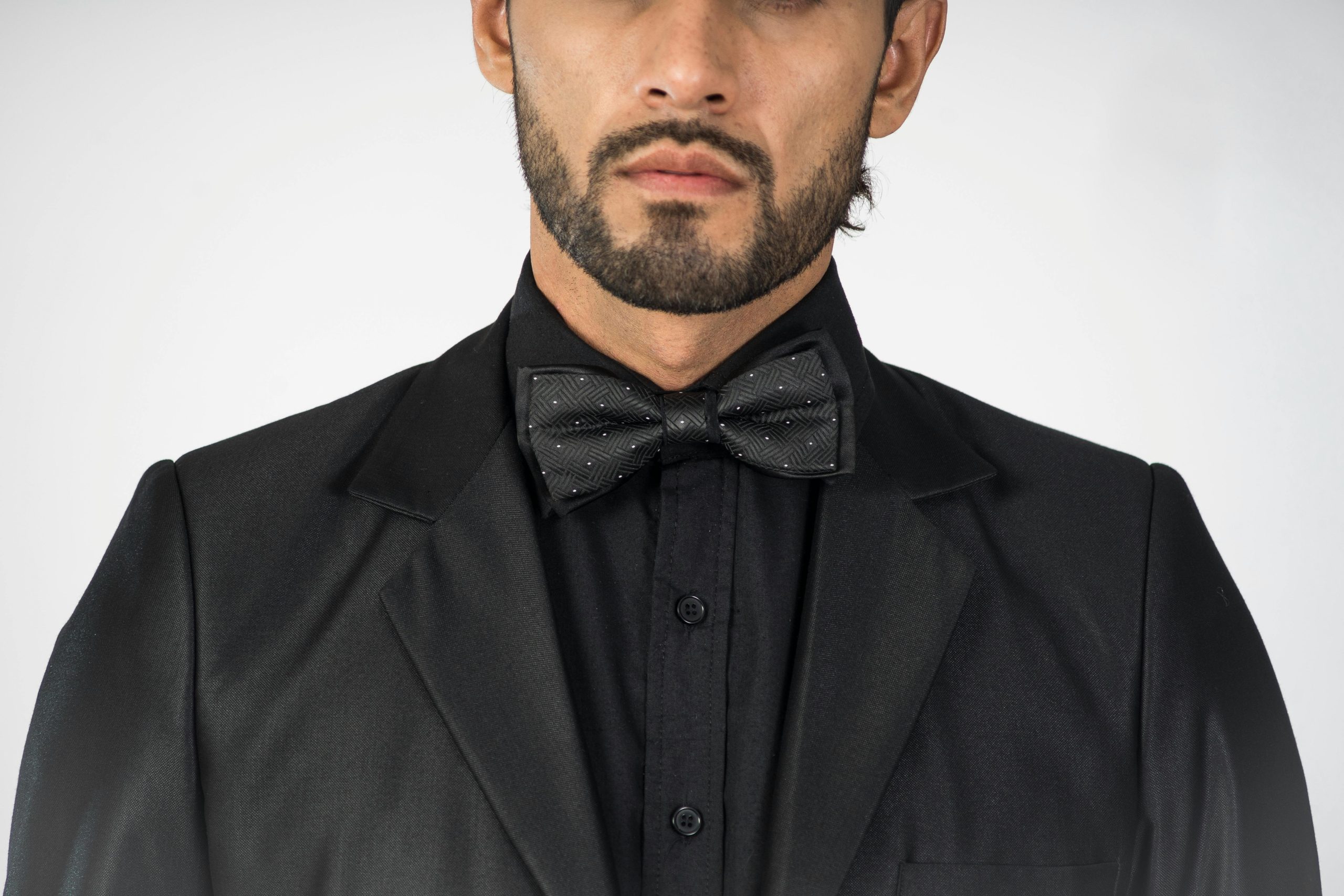 Homme en costume noir avec nœud papillon.