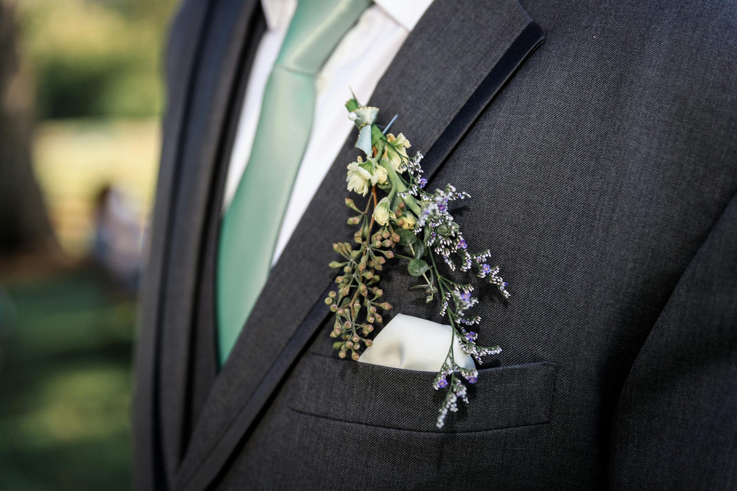 Homme en costume gris avec cravate verte et boutonnière florale.